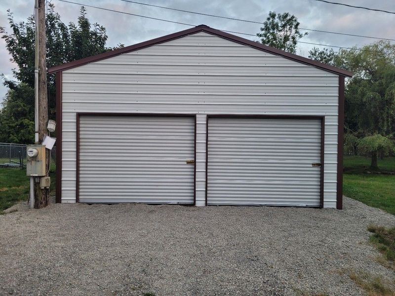 A white garage with two garage doors is sitting on top of a gravel driveway.