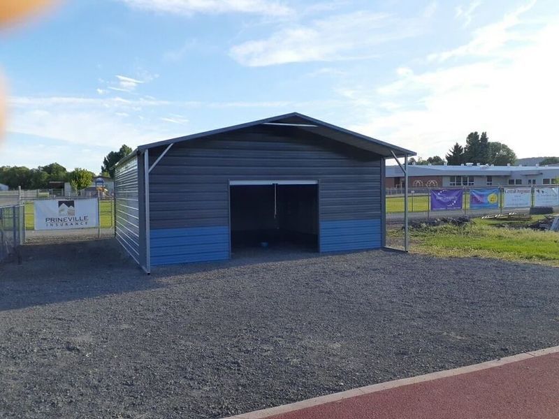 A gray and blue metal building is sitting in a gravel lot next to a track.