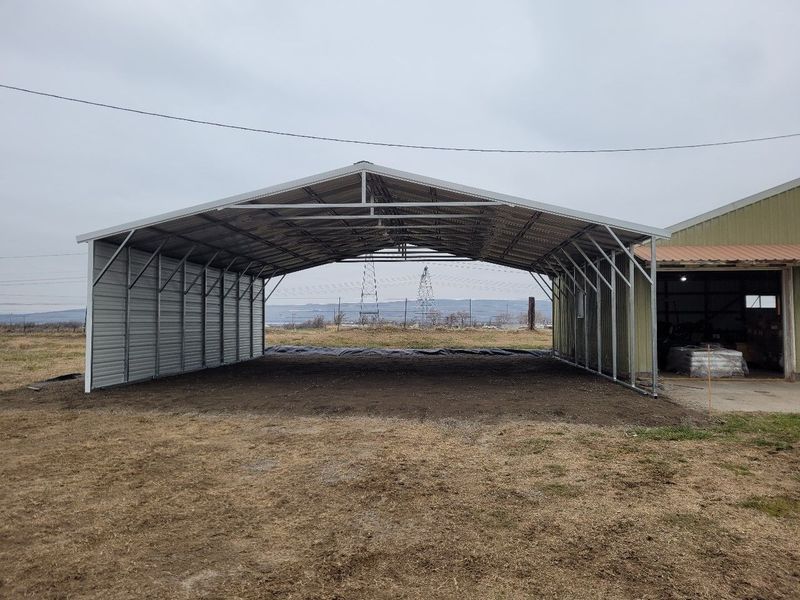 A large metal garage is sitting in the middle of a field.
