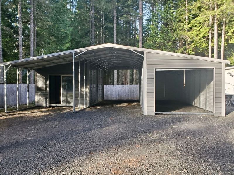 A carport with a garage attached to it in the middle of a forest.