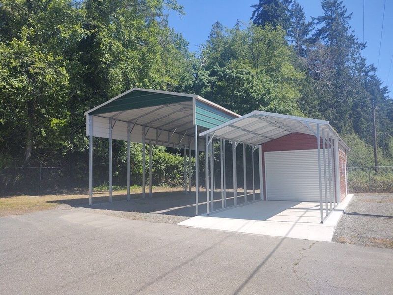 A carport with a green roof next to a garage.
