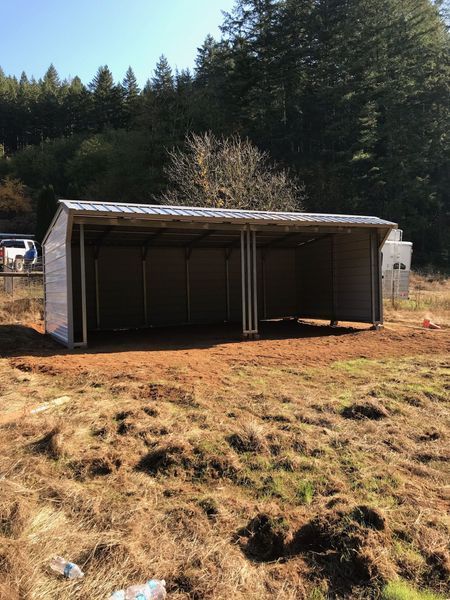A shed is sitting in the middle of a field with trees in the background.