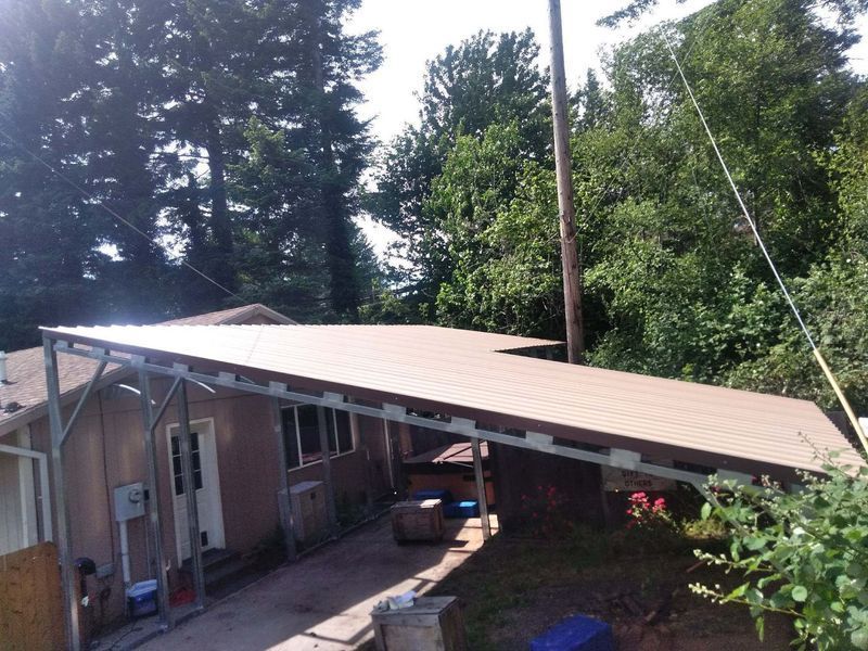 A carport with a brown roof is in front of a house.