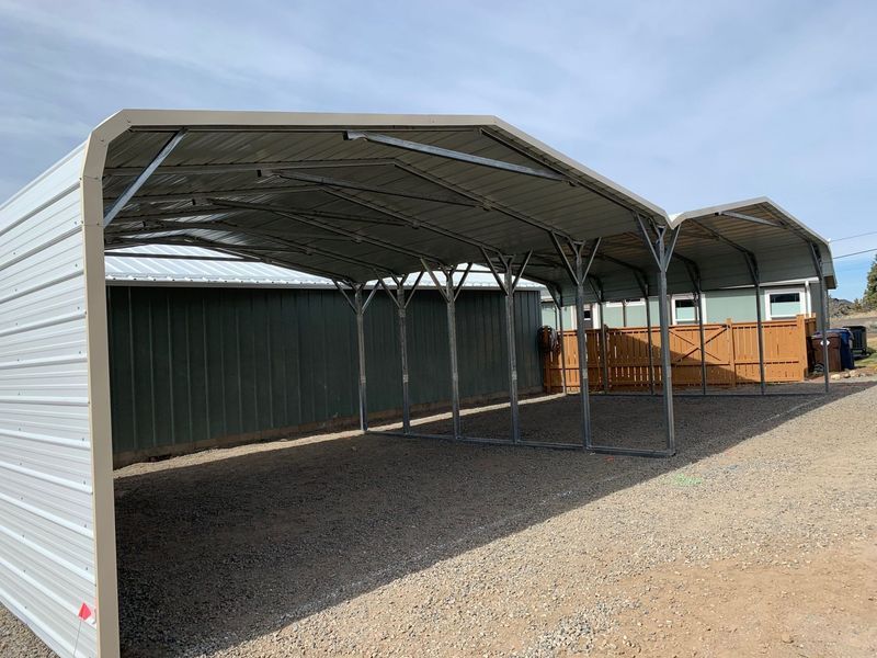 A carport is sitting on top of a gravel road next to a building.