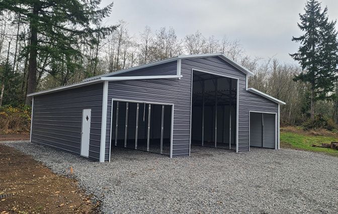 A large metal barn with a garage attached to it is sitting on top of a gravel driveway.
