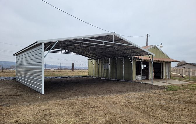 A carport is sitting in the middle of a field next to a house.