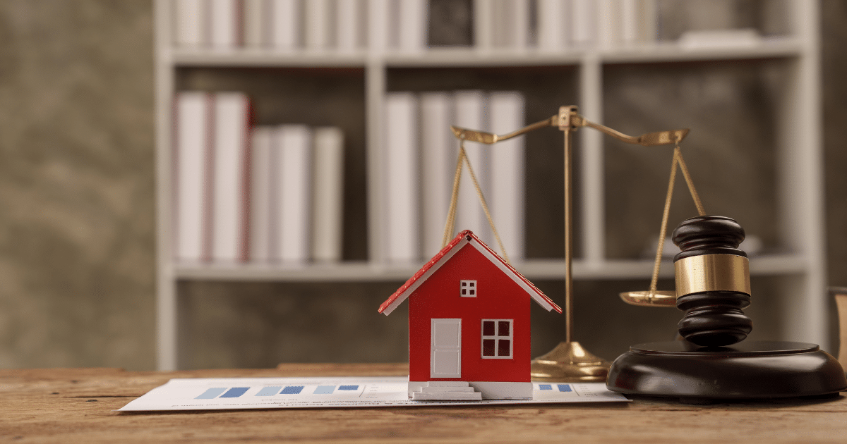 Red house model with a gavel and scales on a desk, symbolizing real estate law and justice
