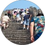 People climbing a stone staircase outdoors with railings and a view of the sky above.