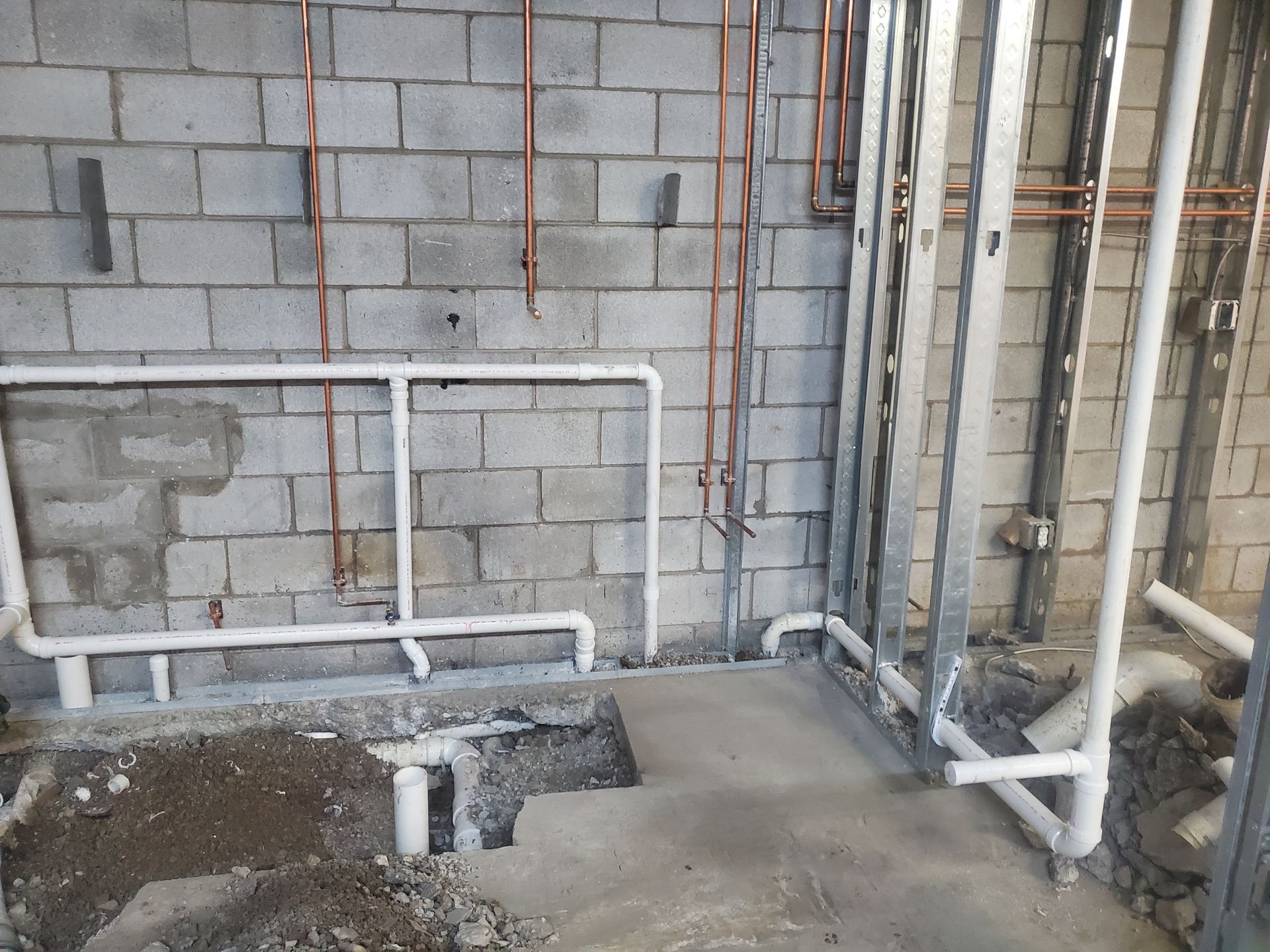 Construction site with cinder block wall, exposed pipes, and a rough floor opening near the wall