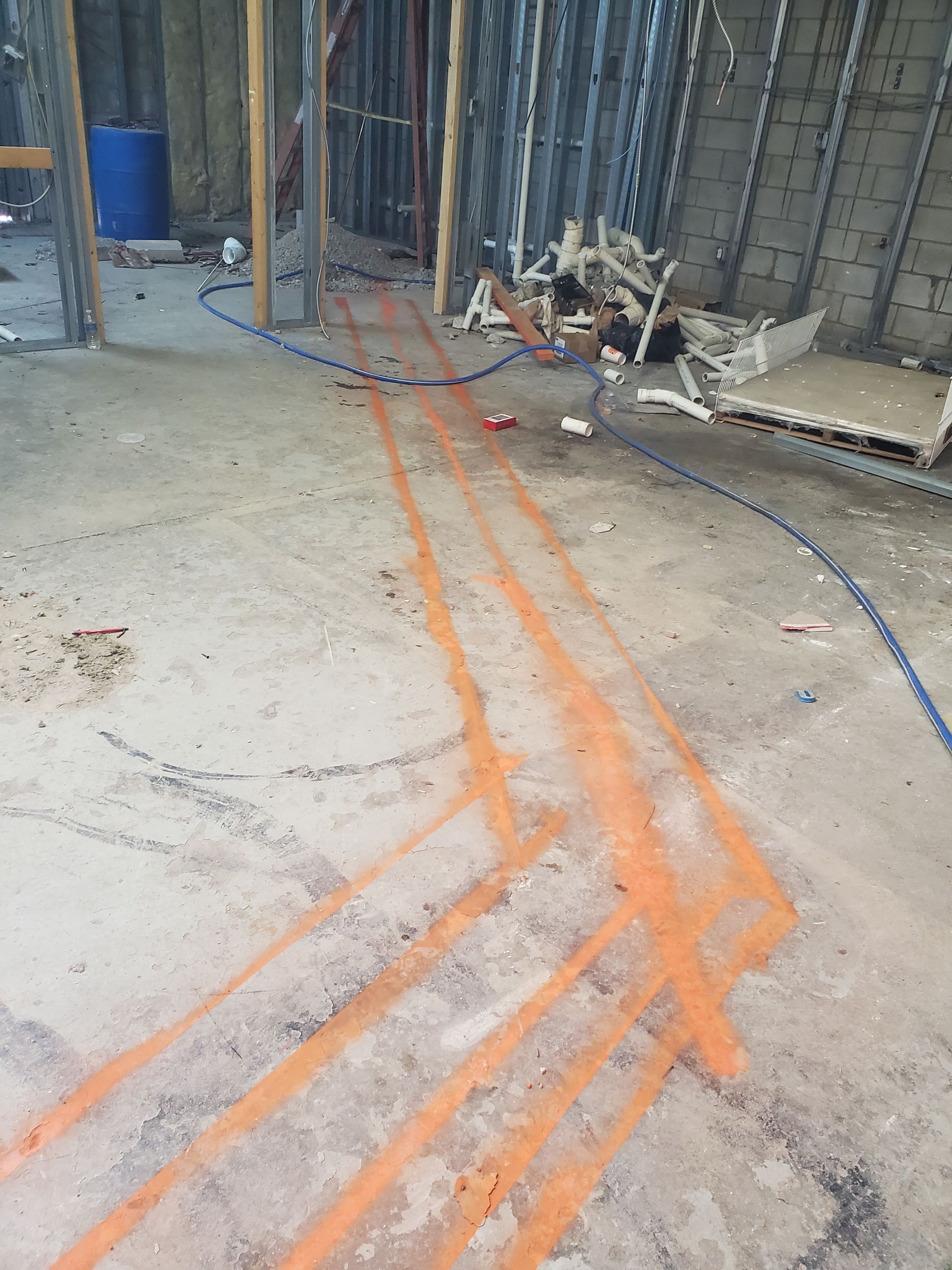 Orange spray-painted utility lines on a concrete floor near a fenced construction area