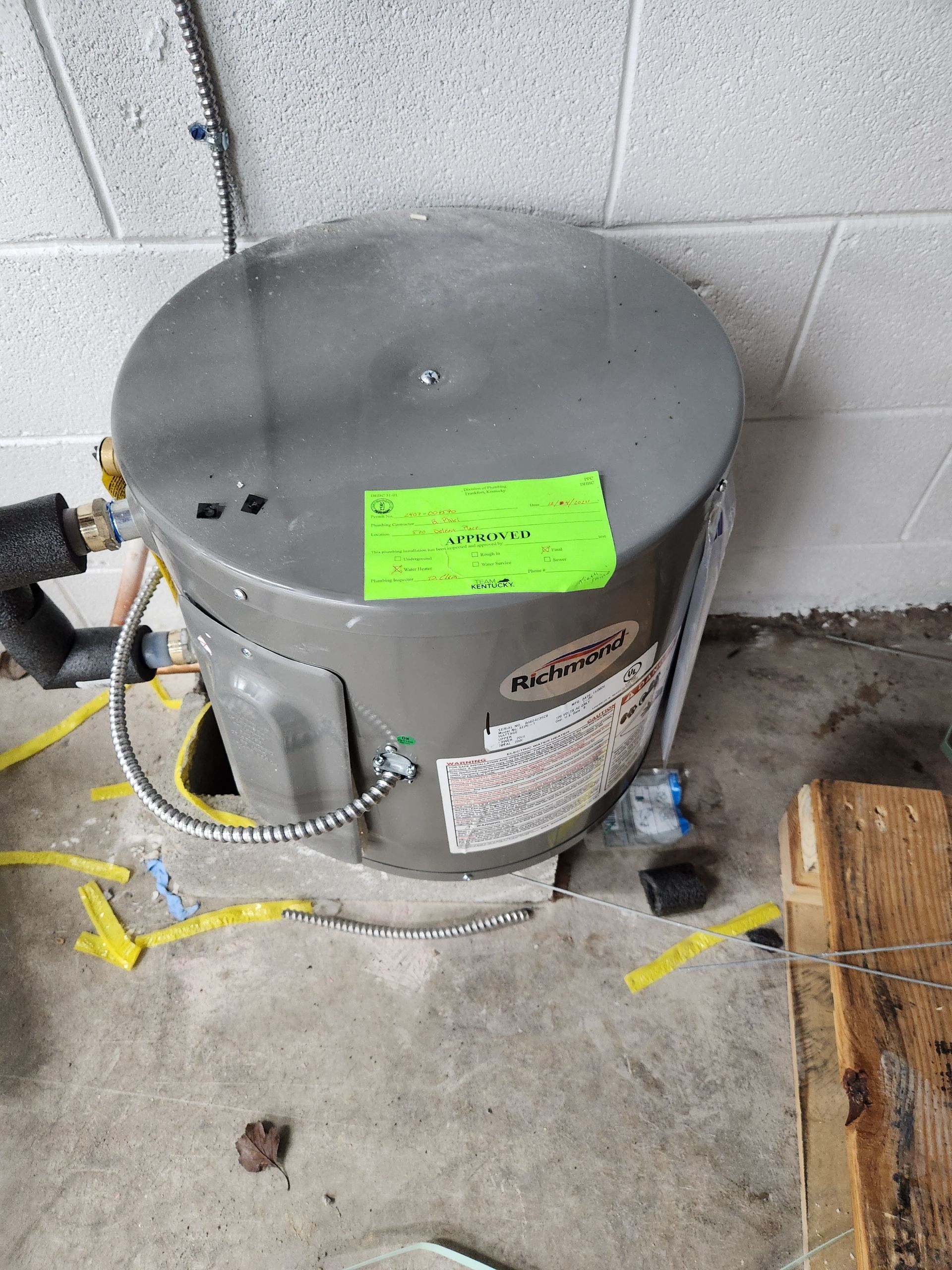 Gray water heater against cinderblock wall with yellow gas line and bright green label on top