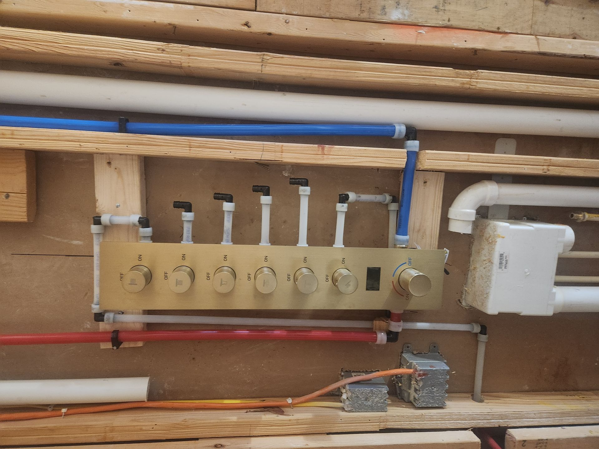 Plumbing manifold with multiple valves and pipes mounted on a wooden wall inside a utility area