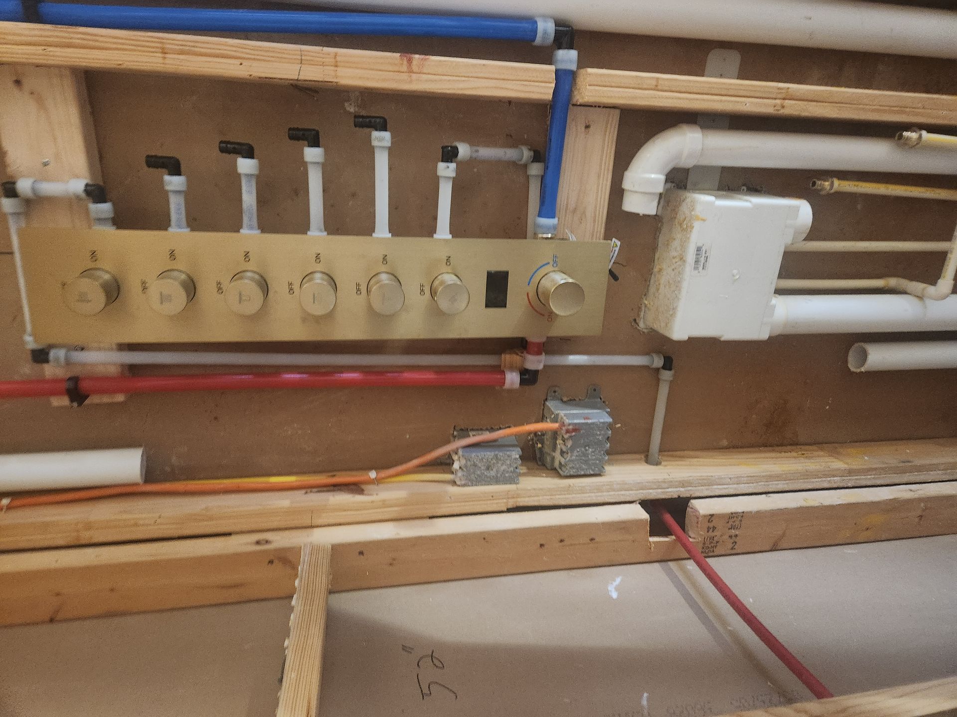 Wall-mounted plumbing controls with pipes, valves, and a small white tank in a utility room