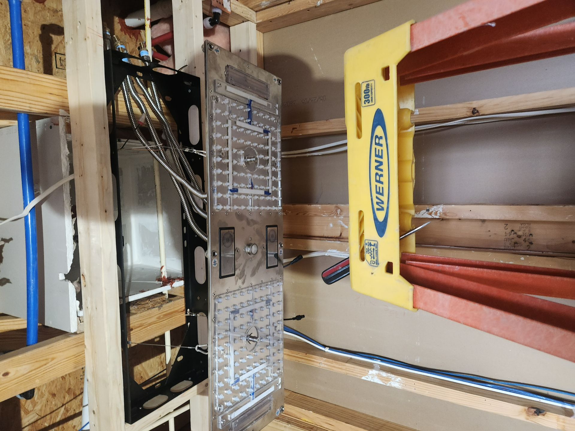 Electrical panel in a workshop wall with open breaker box and yellow clamps nearby
