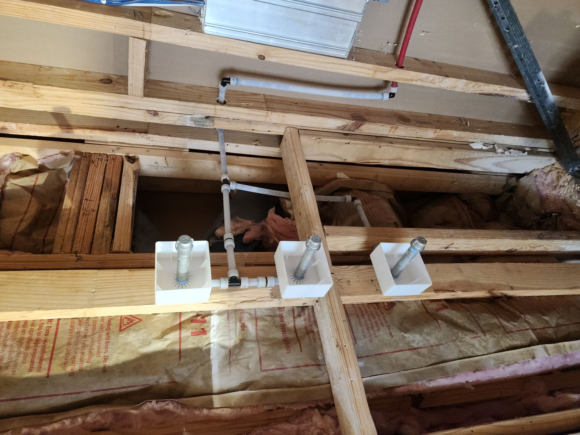 Exposed attic framing with three white electrical boxes mounted on a wooden beam and hanging wires.