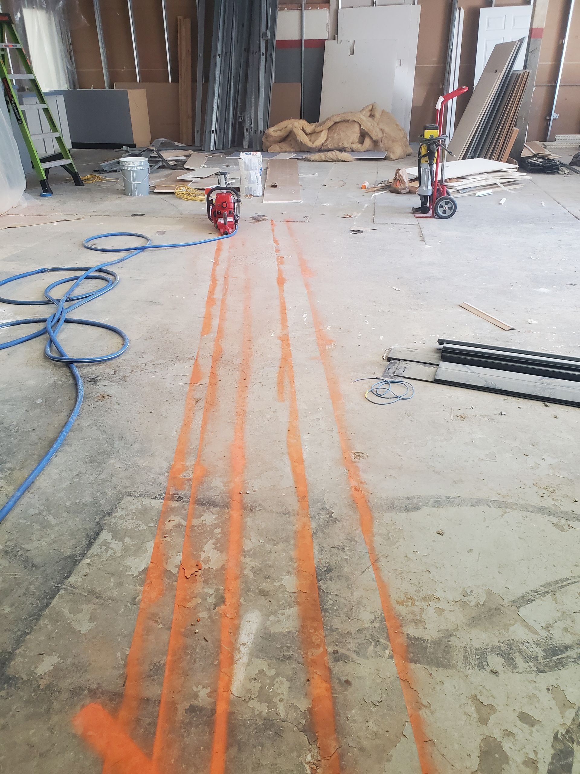 Construction site floor with orange spray markings, hoses, and tools near a work area