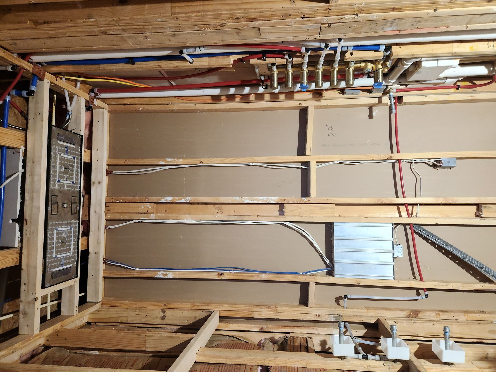 Open wall with exposed wiring, pipes, and wooden framing during construction or renovation.