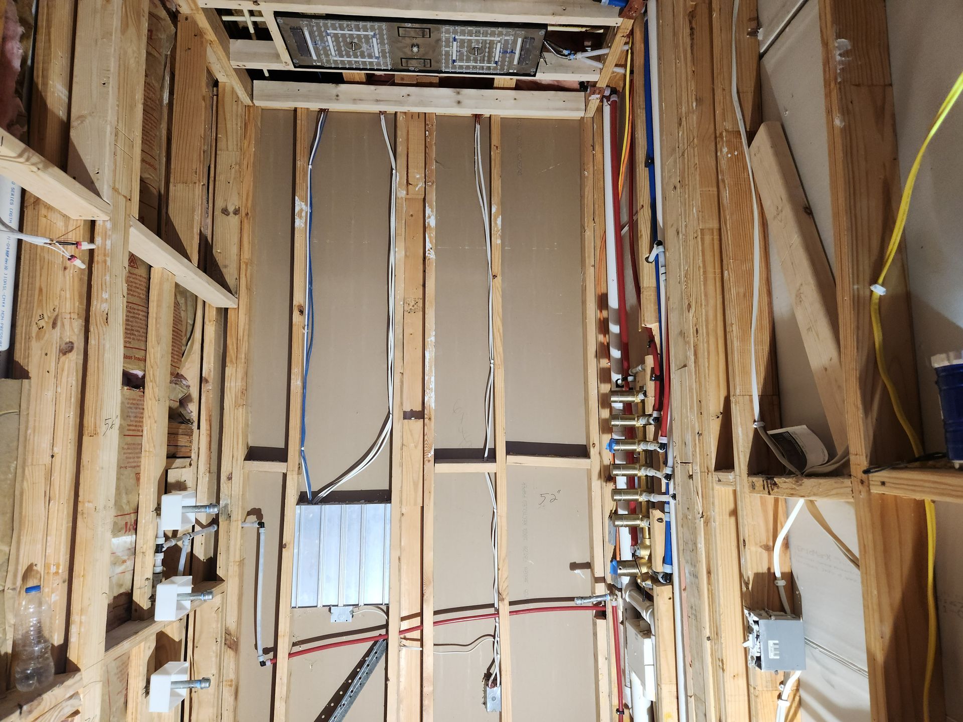 Unfinished room with exposed wall studs, wiring, and a ladder in the center.
