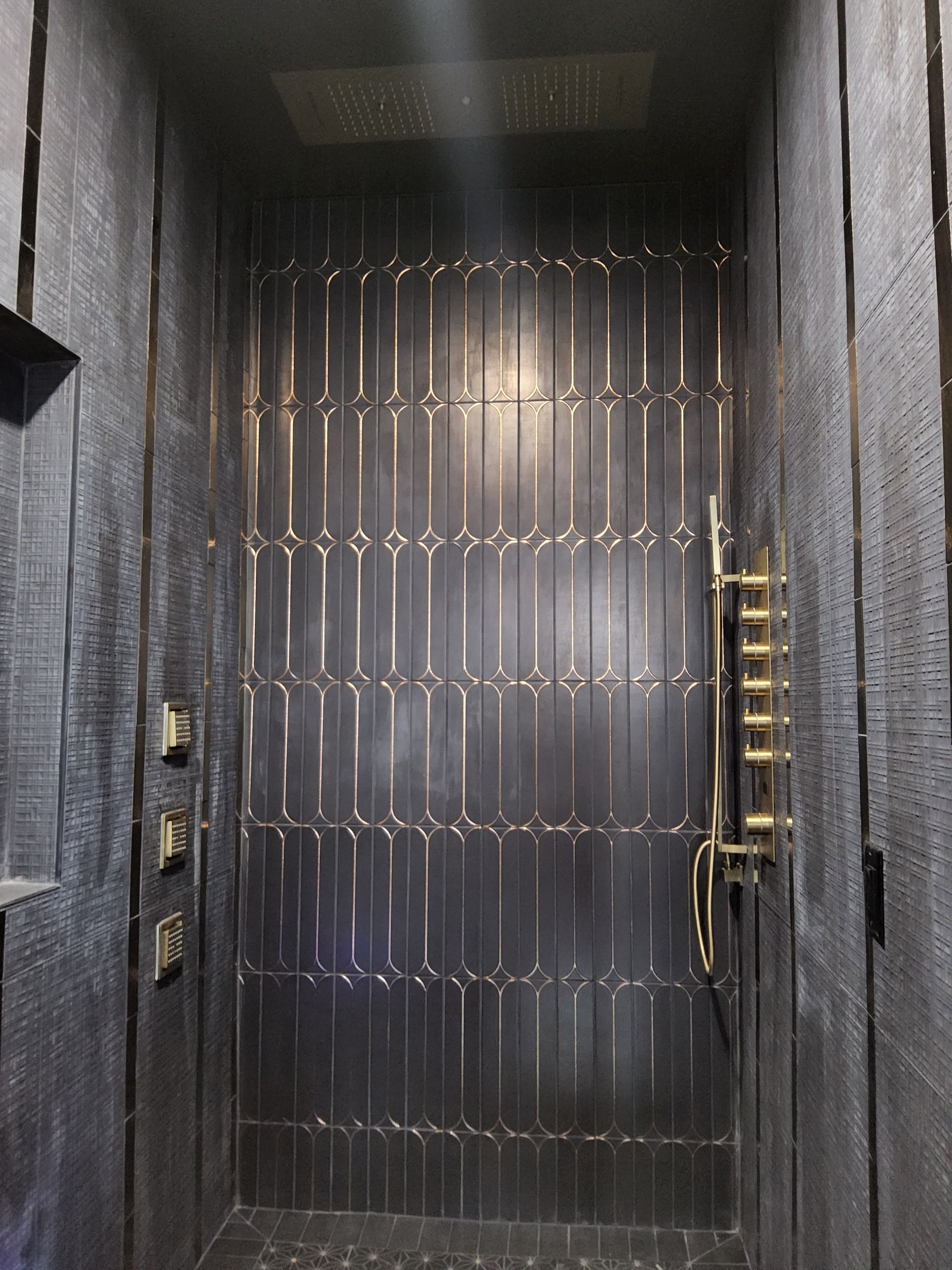 Dark metal front door with vertical ridges and brass handles in a dim entryway