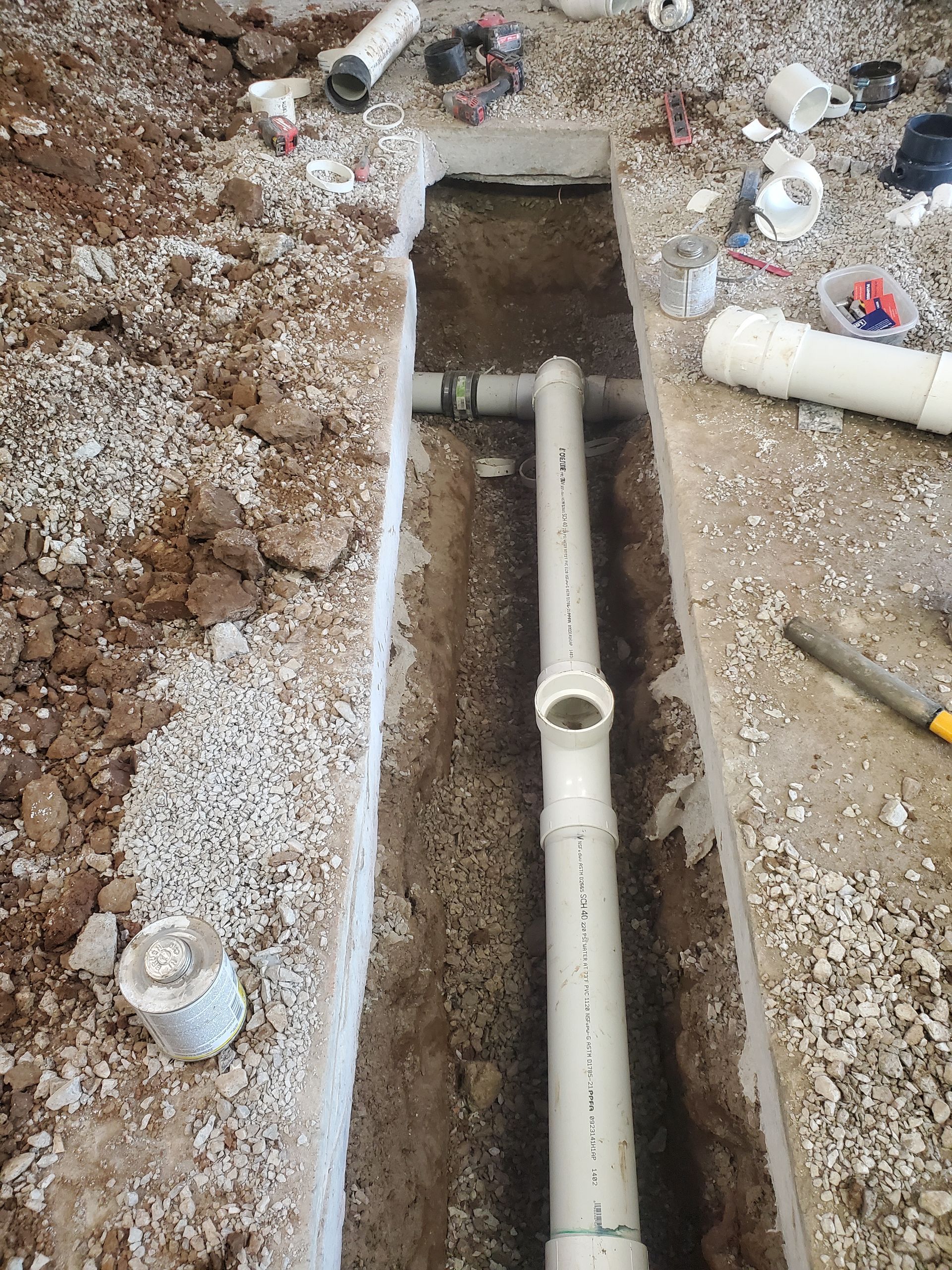 Trench with exposed white PVC pipes in a dirt excavation site, with debris scattered around.