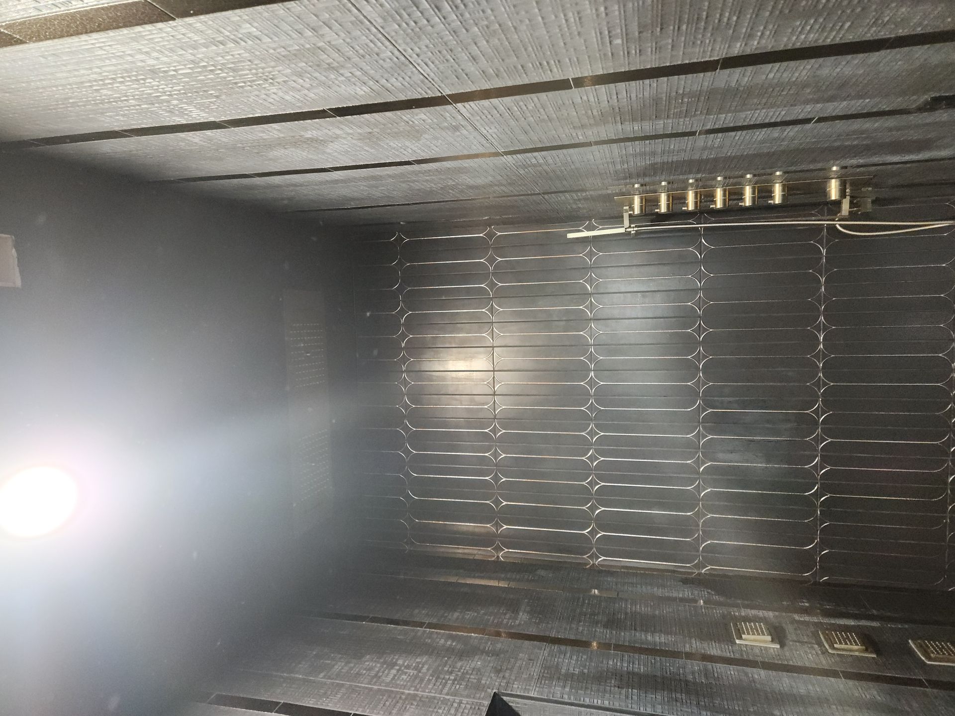 Dim industrial interior with a bright light on the left and metal grates along the wall.