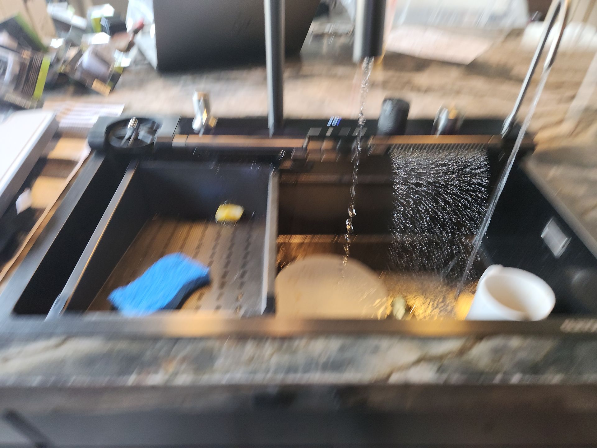 Stainless steel kitchen sink with dishes, sponge, and water spraying into the basin