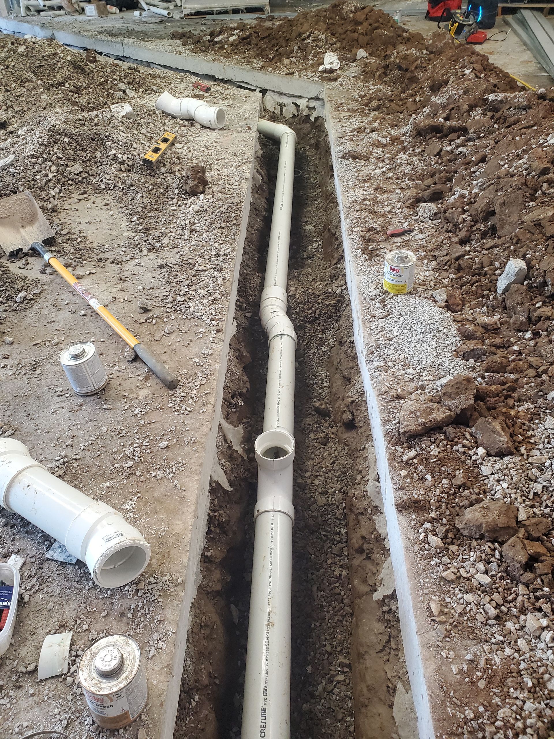 Open trench with white PVC drainage pipes laid in gravel during construction work