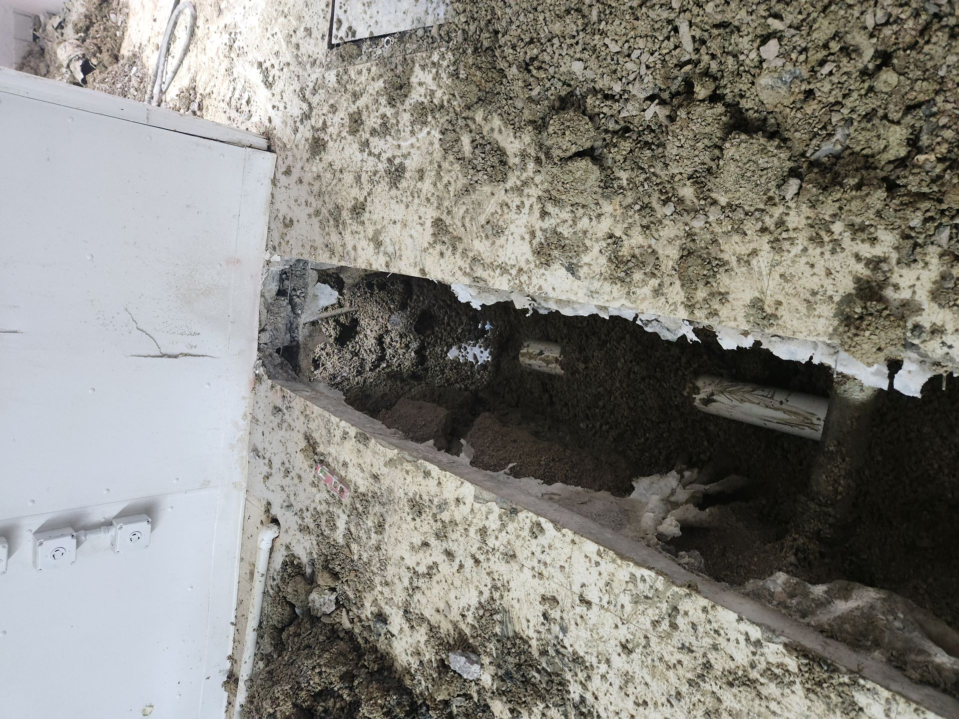 Damaged wall with a large broken opening exposing a dark cavity next to a white door.