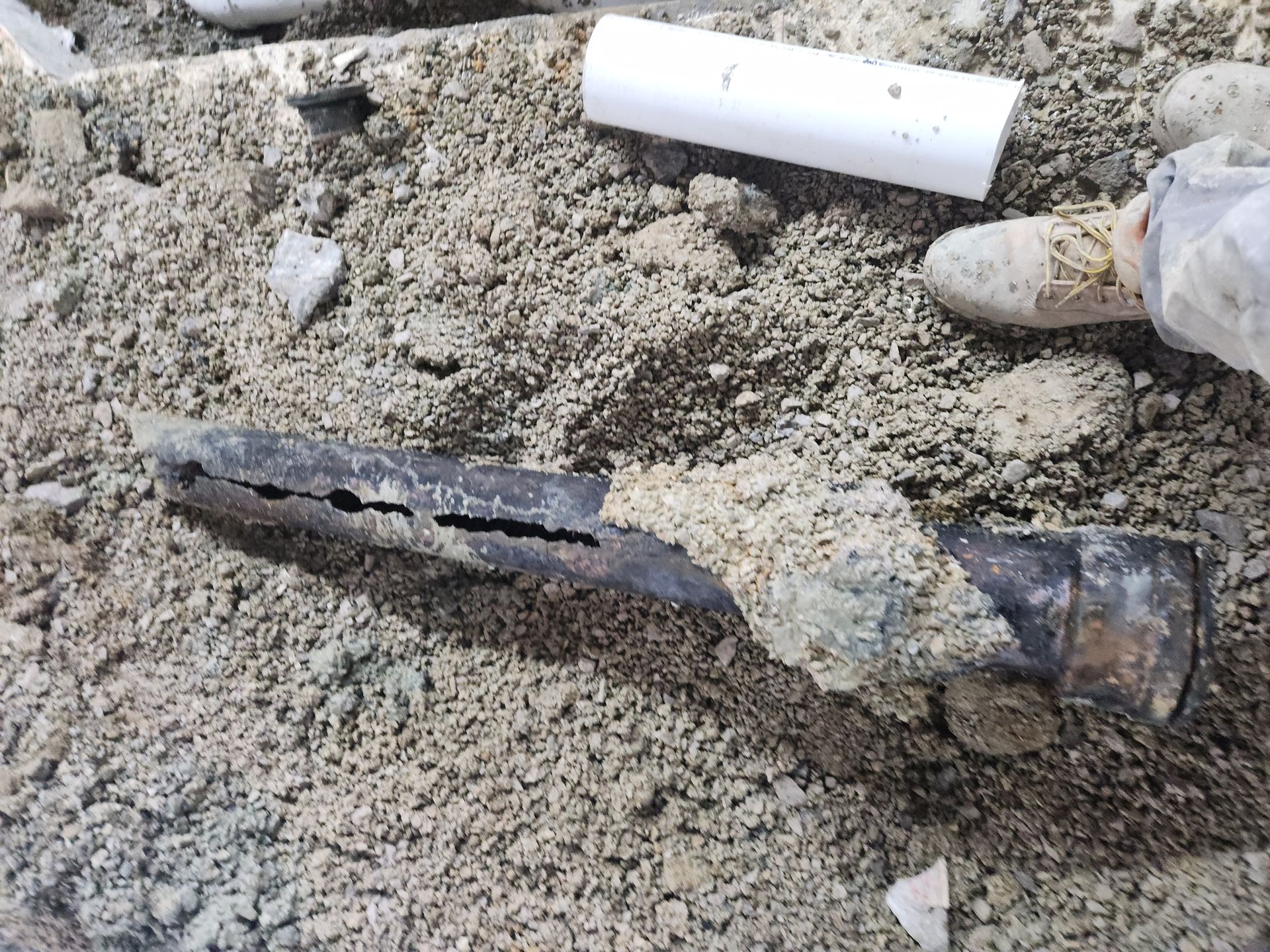 Broken rusty pipe partially buried in sand and dirt, with debris nearby
