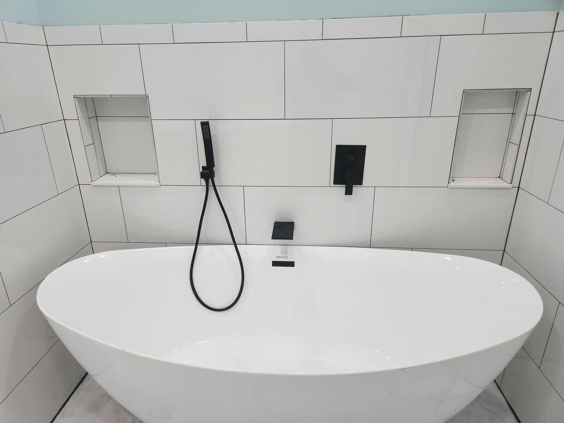 Modern white bathroom with oval bathtub, black faucet, and tiled wall niches