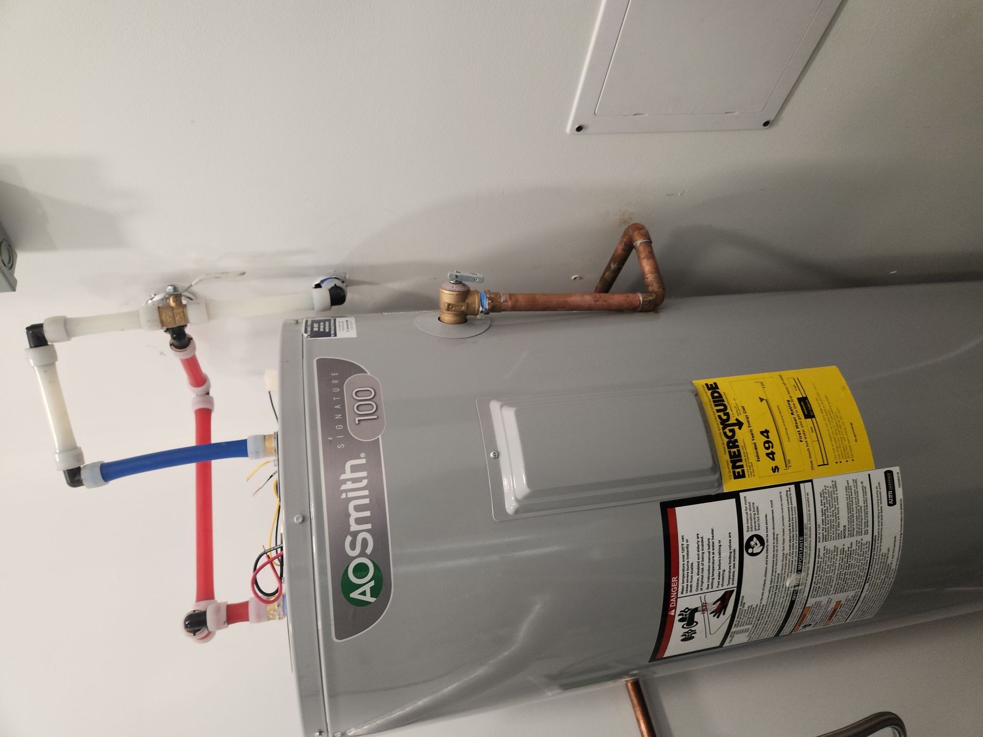 Gray water heater with copper piping and red/blue shutoff valves in a utility closet.