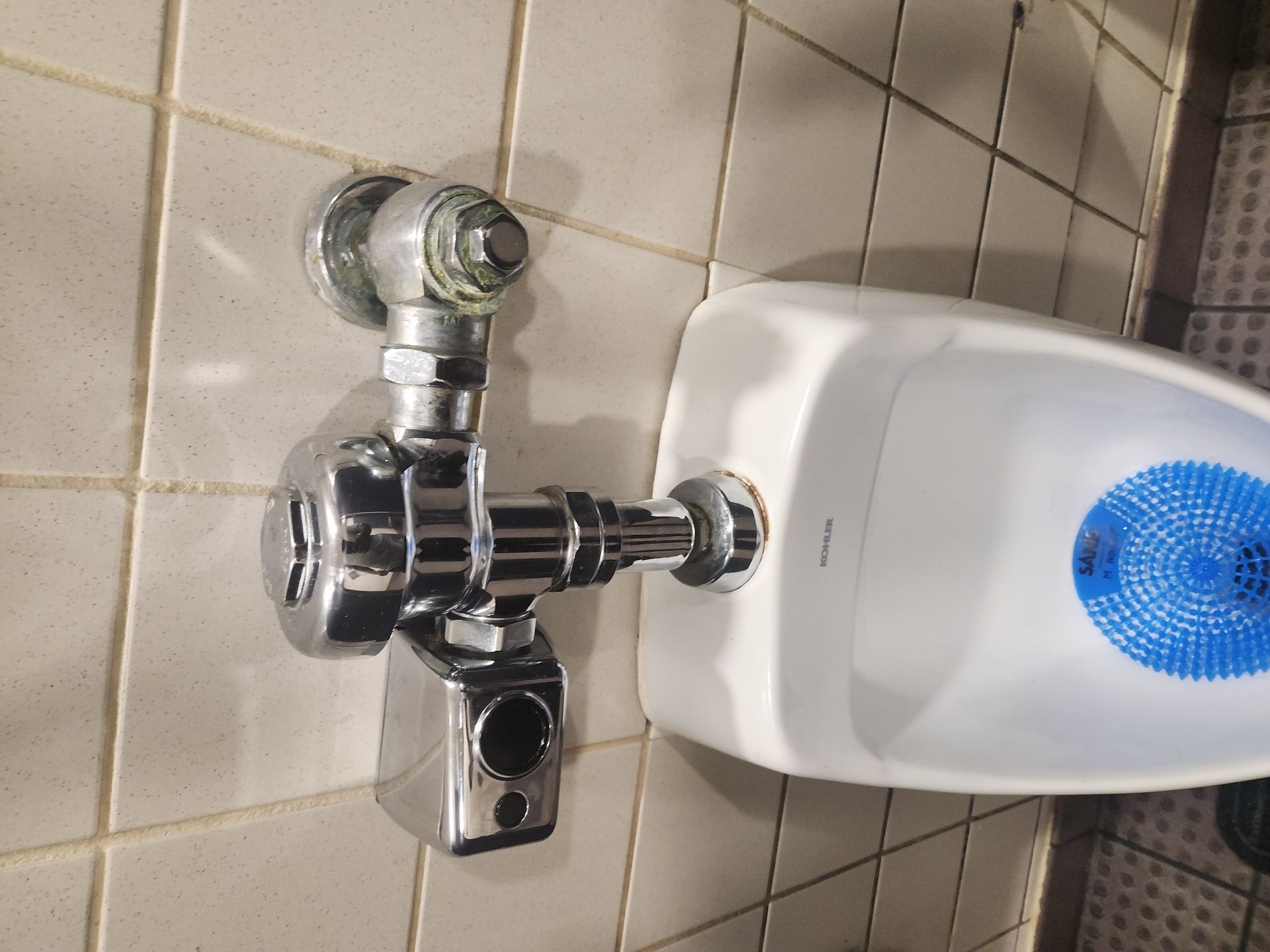 Chrome wall-mounted bathroom faucet beside a white hand dryer and tiled wall.