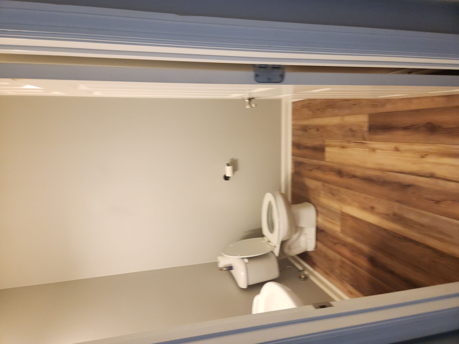 Small bathroom with a toilet beside a wood-paneled wall and beige tile floor.