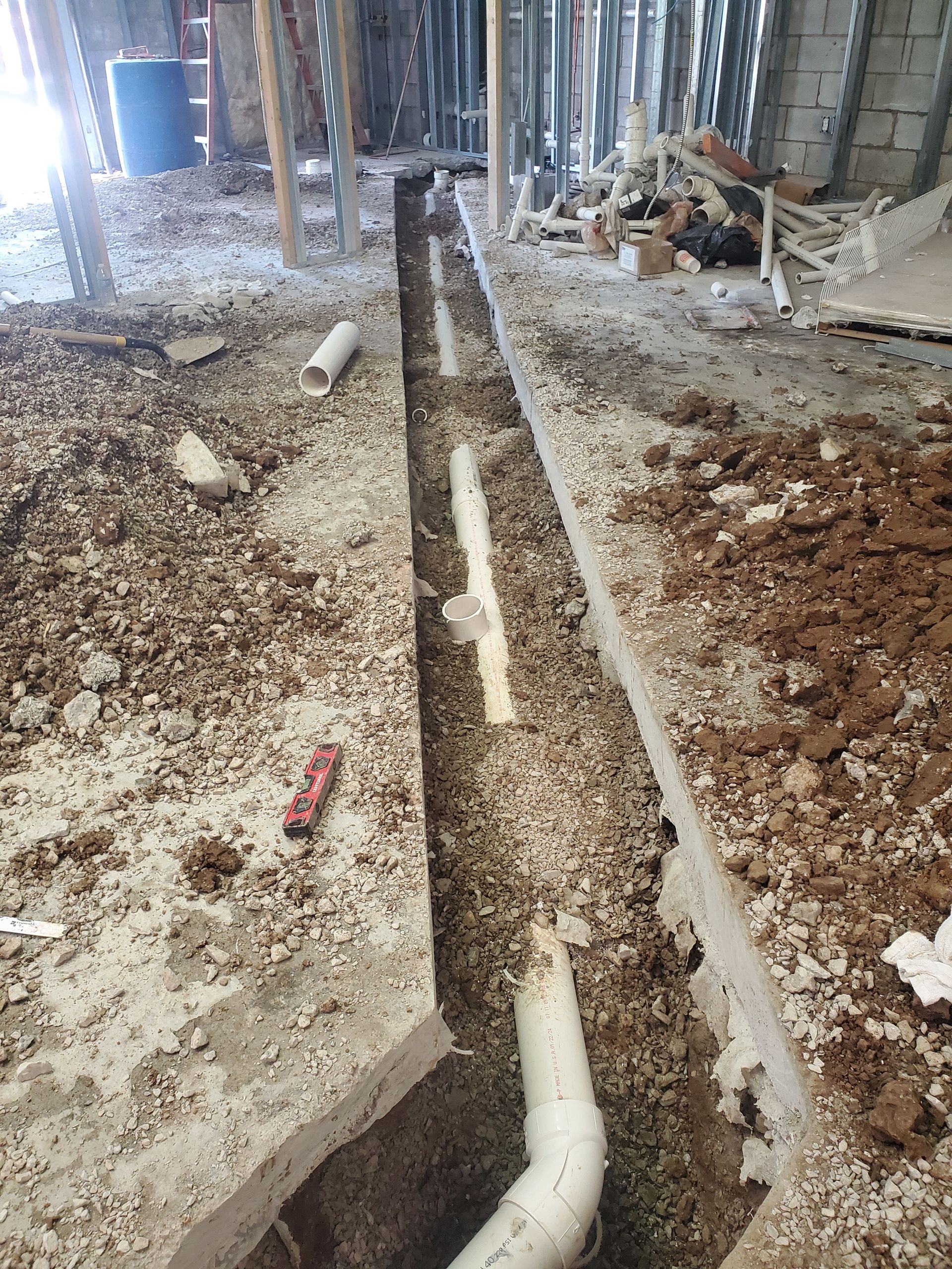 Construction trench with exposed white pipe running through a dirt floor inside a building under renovation