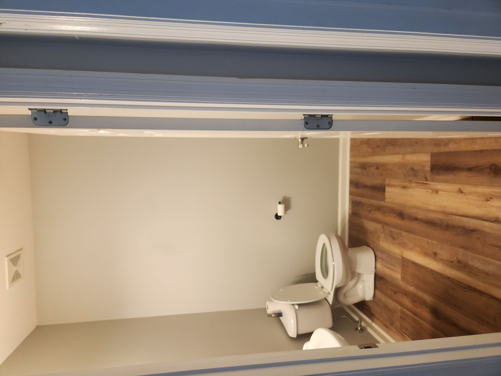 Upside-down view of a bathroom with a toilet, beige walls, and wood-look flooring.