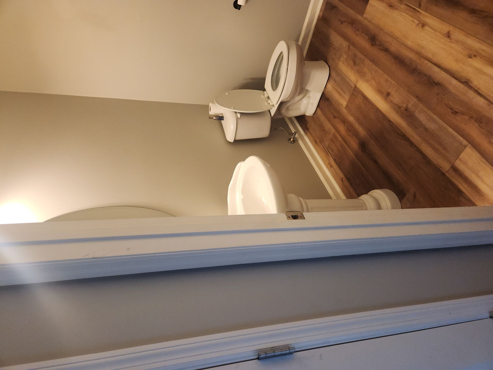 Bathroom with a toilet, sink, and beige walls viewed through a doorway.