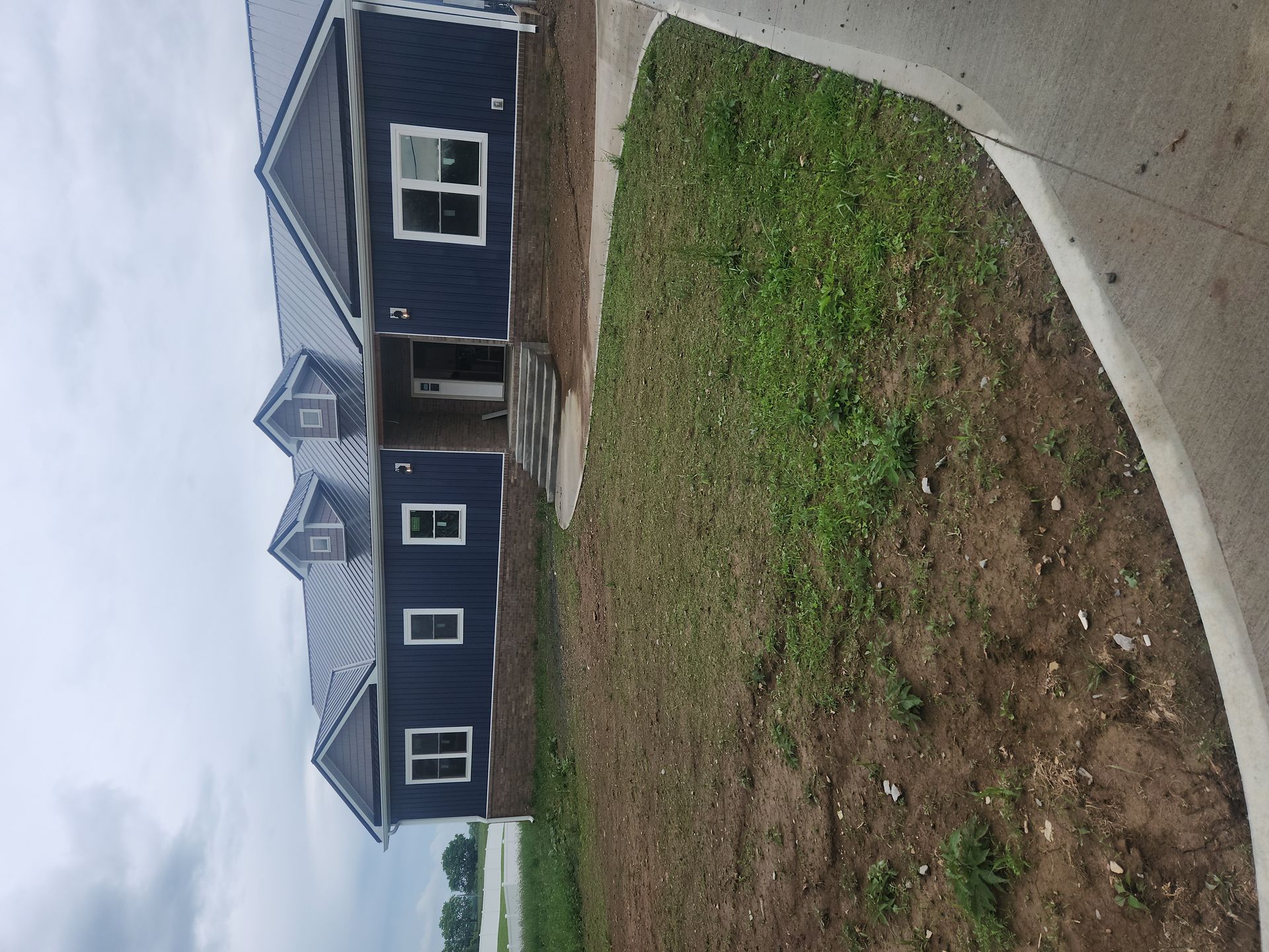 New house with dark siding and white trim, seen from a curved concrete driveway beside a bare yard
