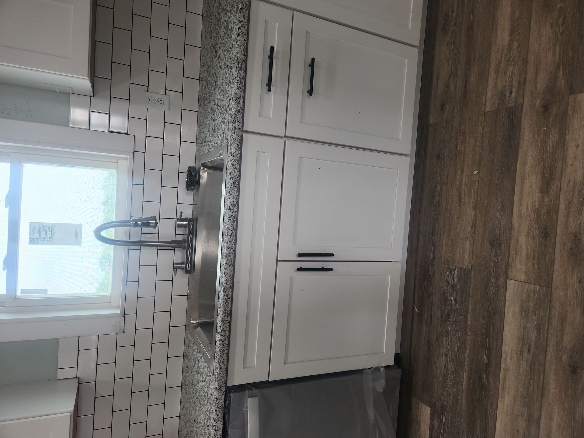 Modern kitchen with white cabinets, granite countertop, subway tile backsplash, and wood-look flooring