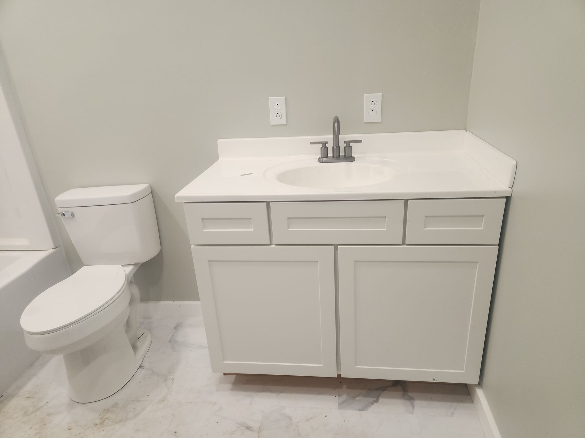 Small bathroom with white toilet and vanity sink against a light gray wall.