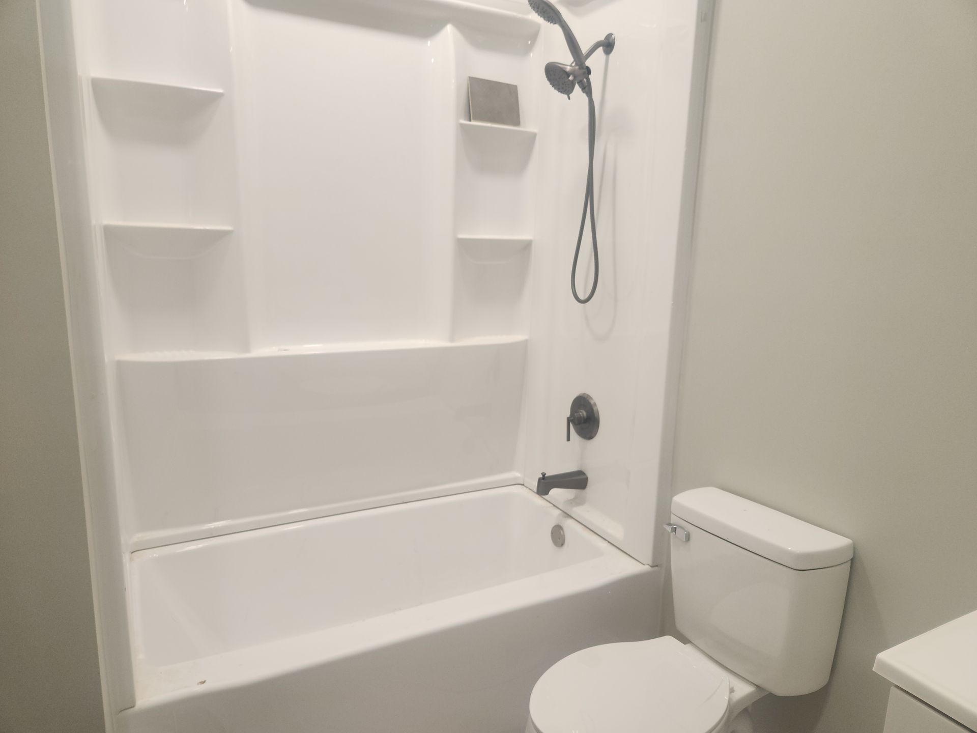 Accessible white bathtub and shower with grab bars, showerhead, and toilet in a small bathroom.