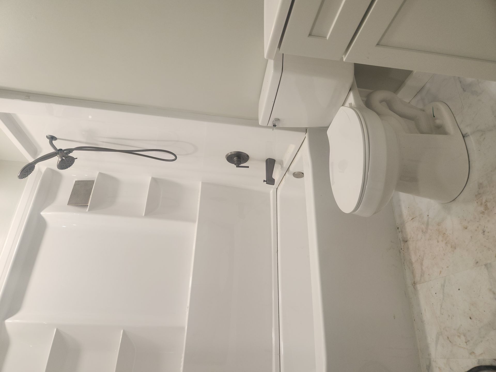 White bathroom with a showerhead, shelves, and a sink next to a tiled wall.