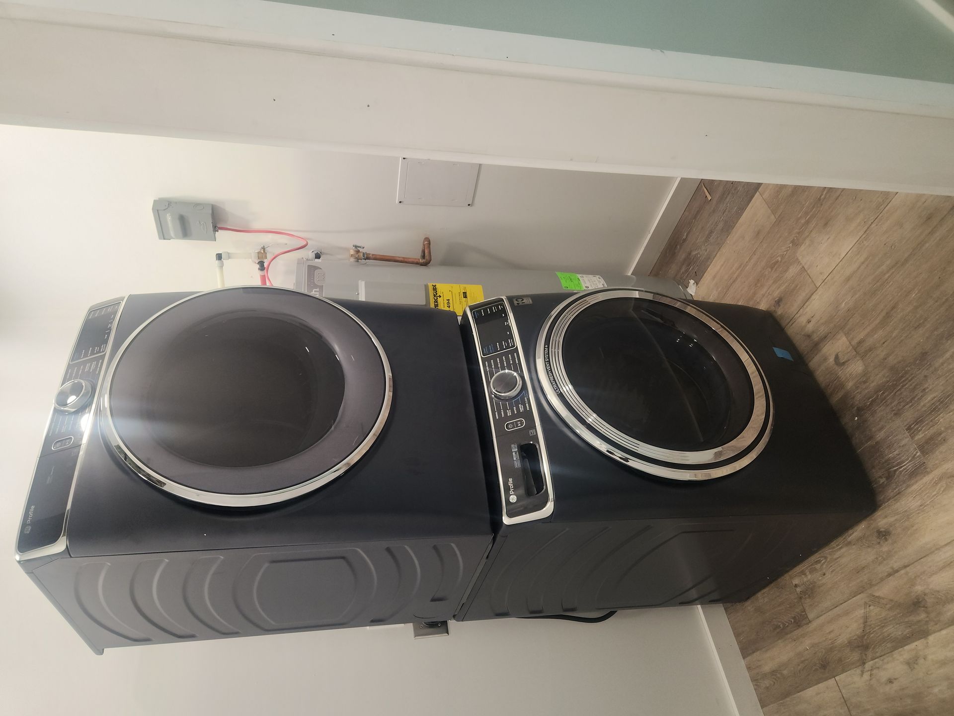 Two stacked black laundry machines in a room with wood flooring and white walls.