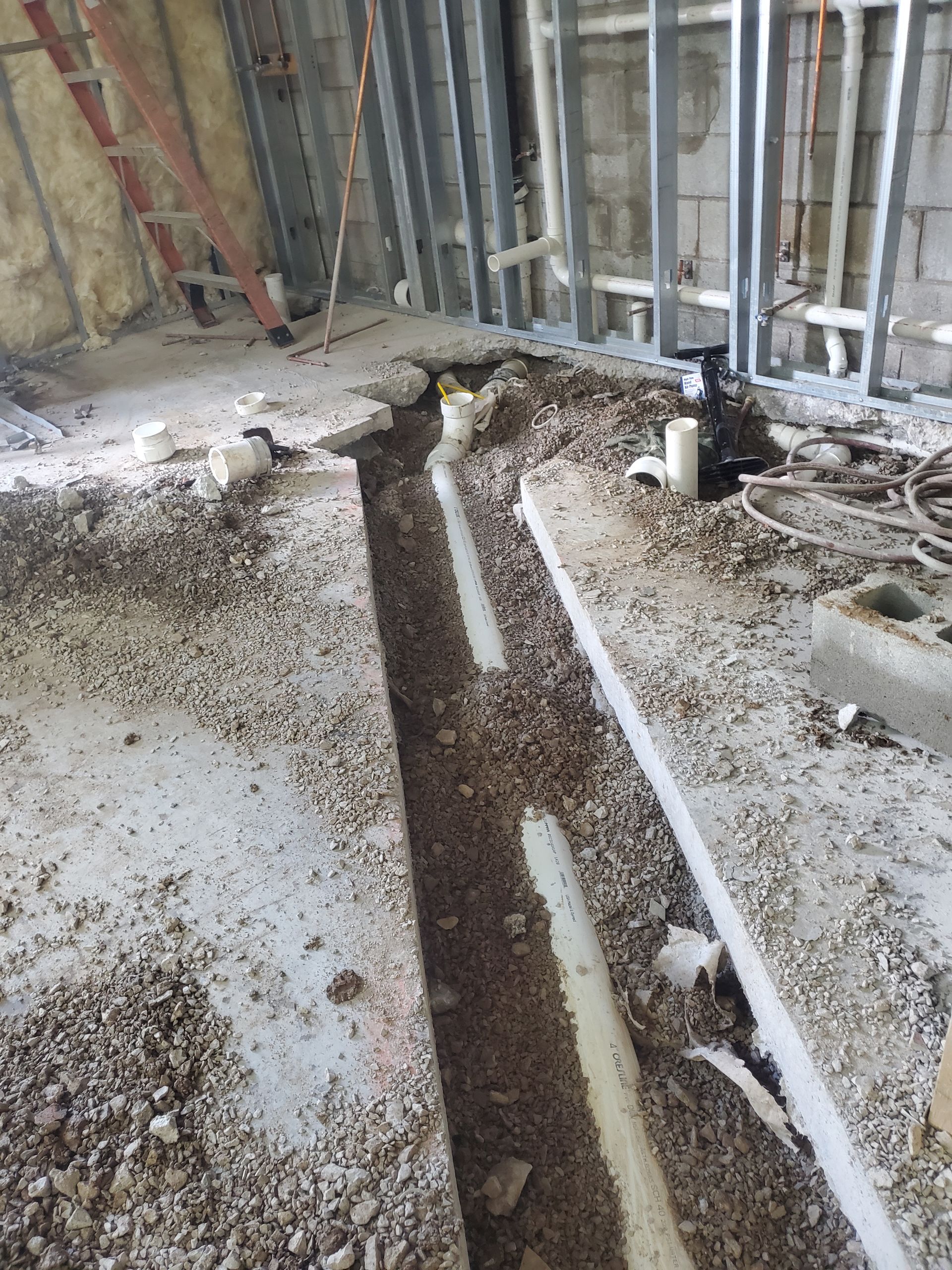 Construction site floor with a long trench cut into concrete and exposed wall framing.