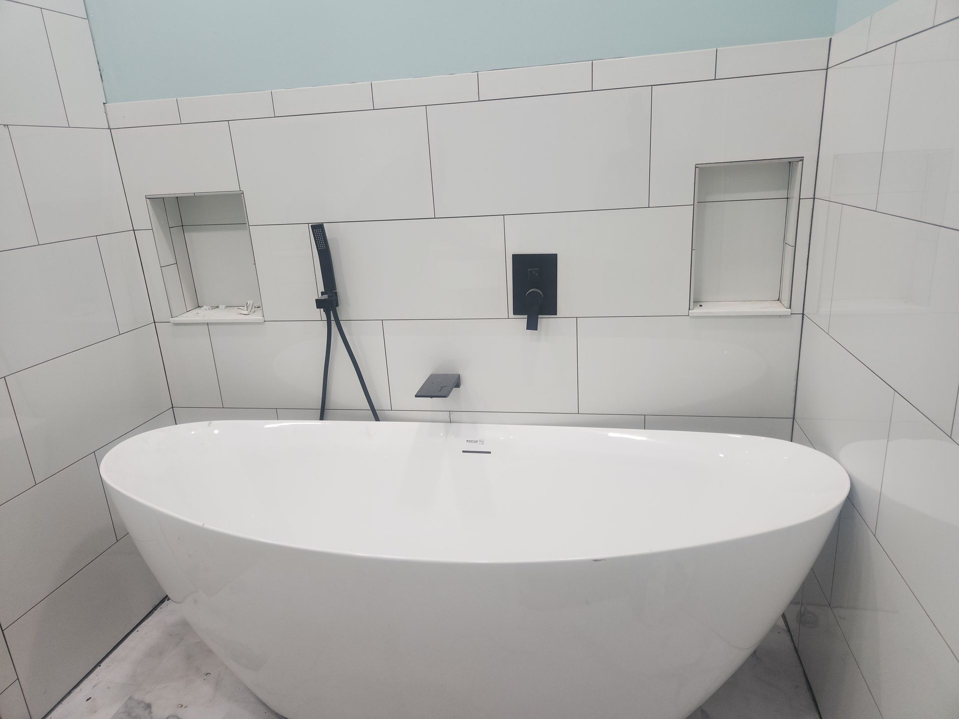 Modern bathroom with a freestanding white bathtub, tiled walls, and black fixtures