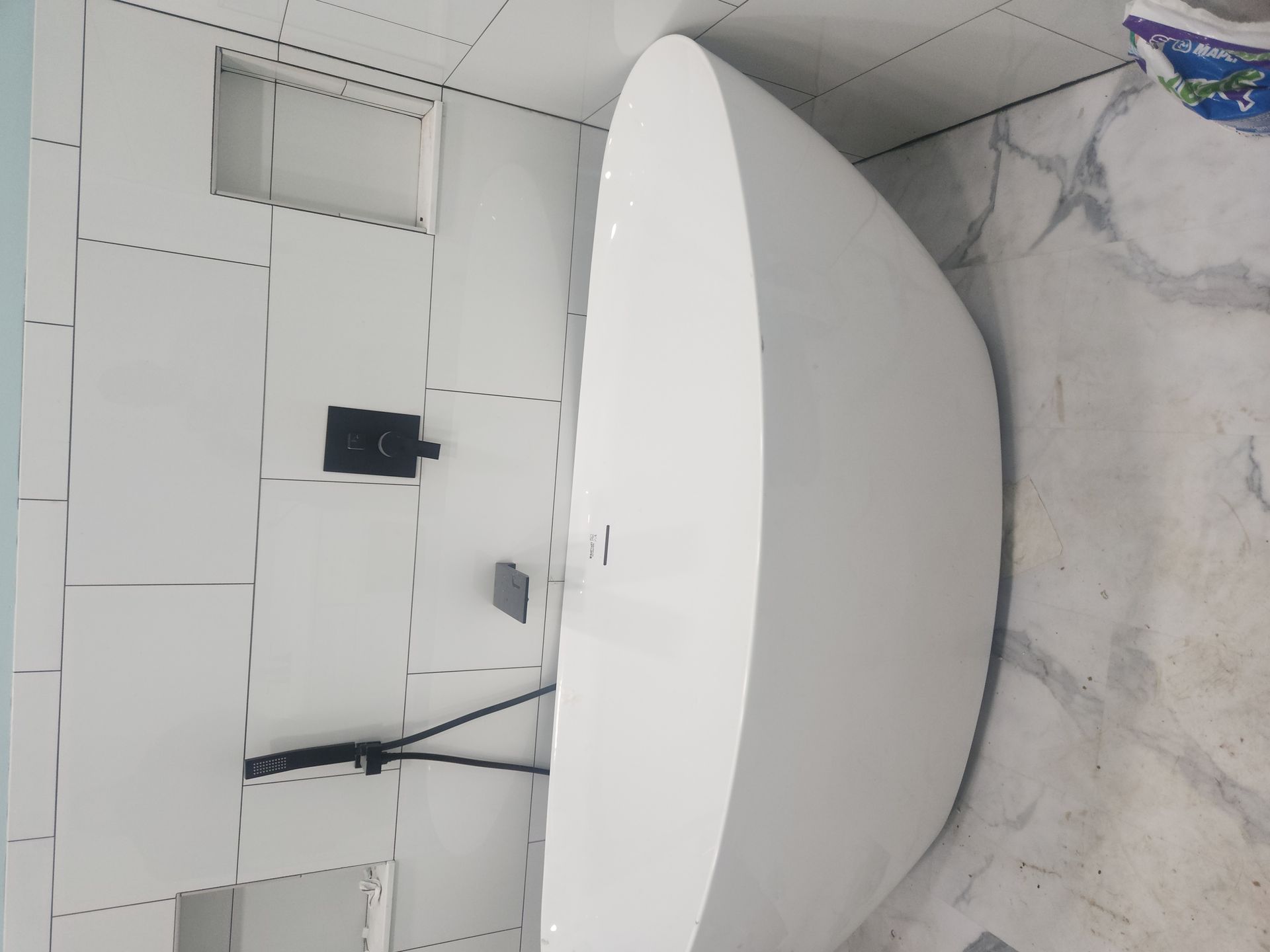 White freestanding bathtub in a tiled bathroom with a marble-look floor and wall-mounted faucet