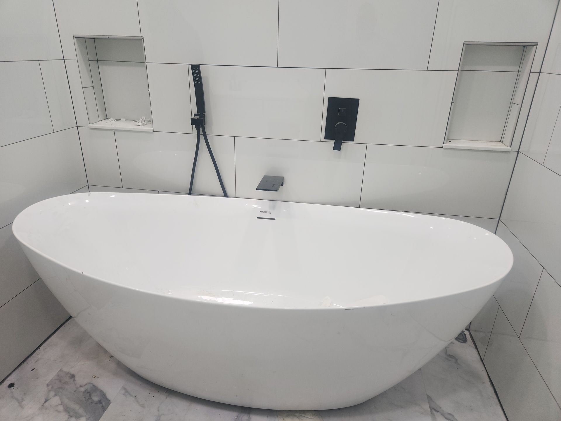 Modern freestanding white bathtub in a tiled bathroom alcove