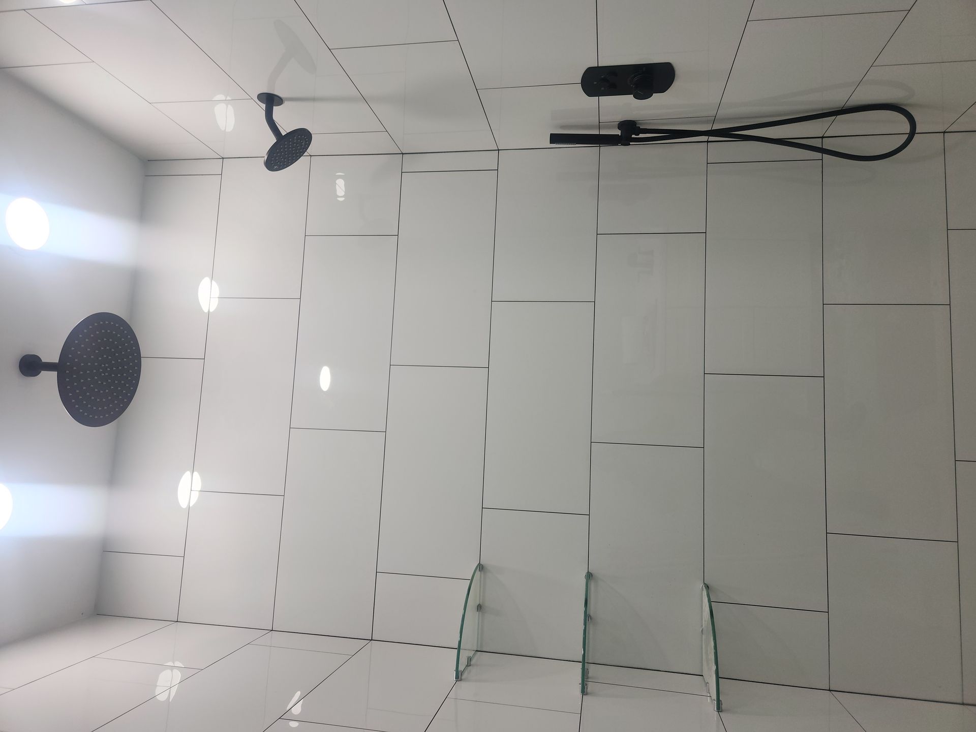 White tiled shower with black fixtures, overhead rain shower, and glass door.