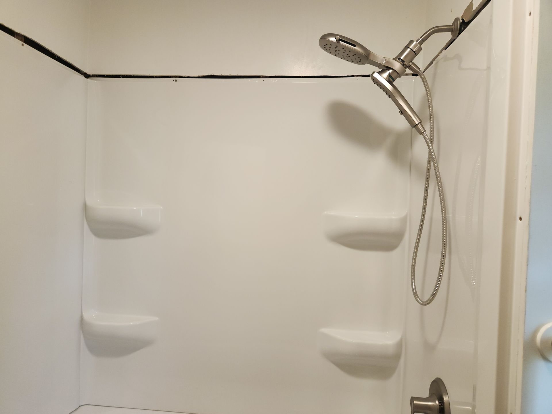 Empty white shower stall with built-in shelves and a handheld showerhead on the right