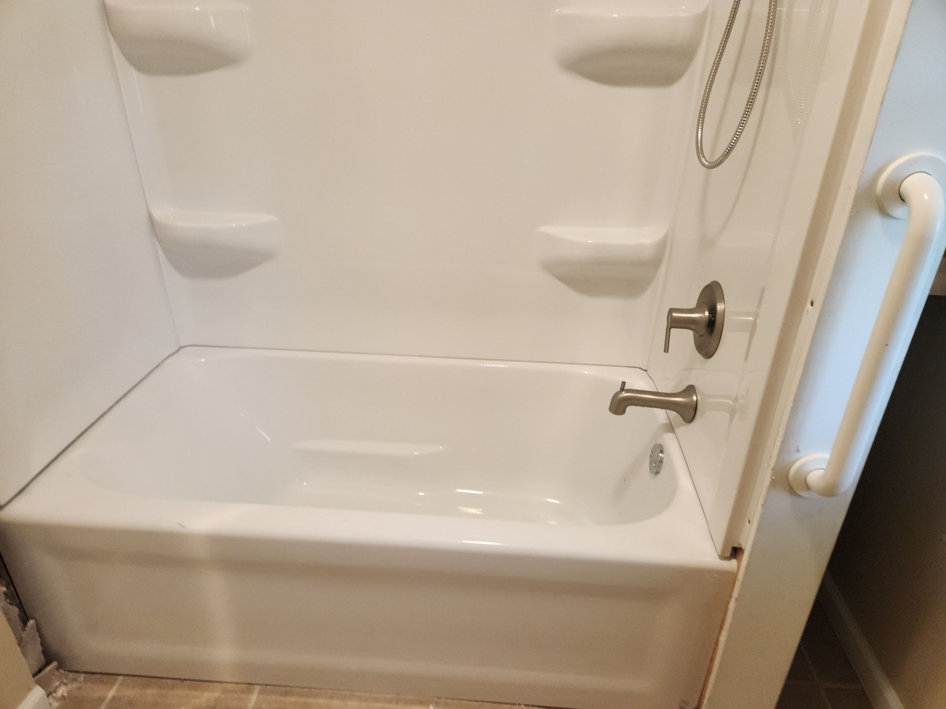 Empty white accessible shower with grab bars, wall-mounted seat, and handheld showerhead in a tiled bathroom