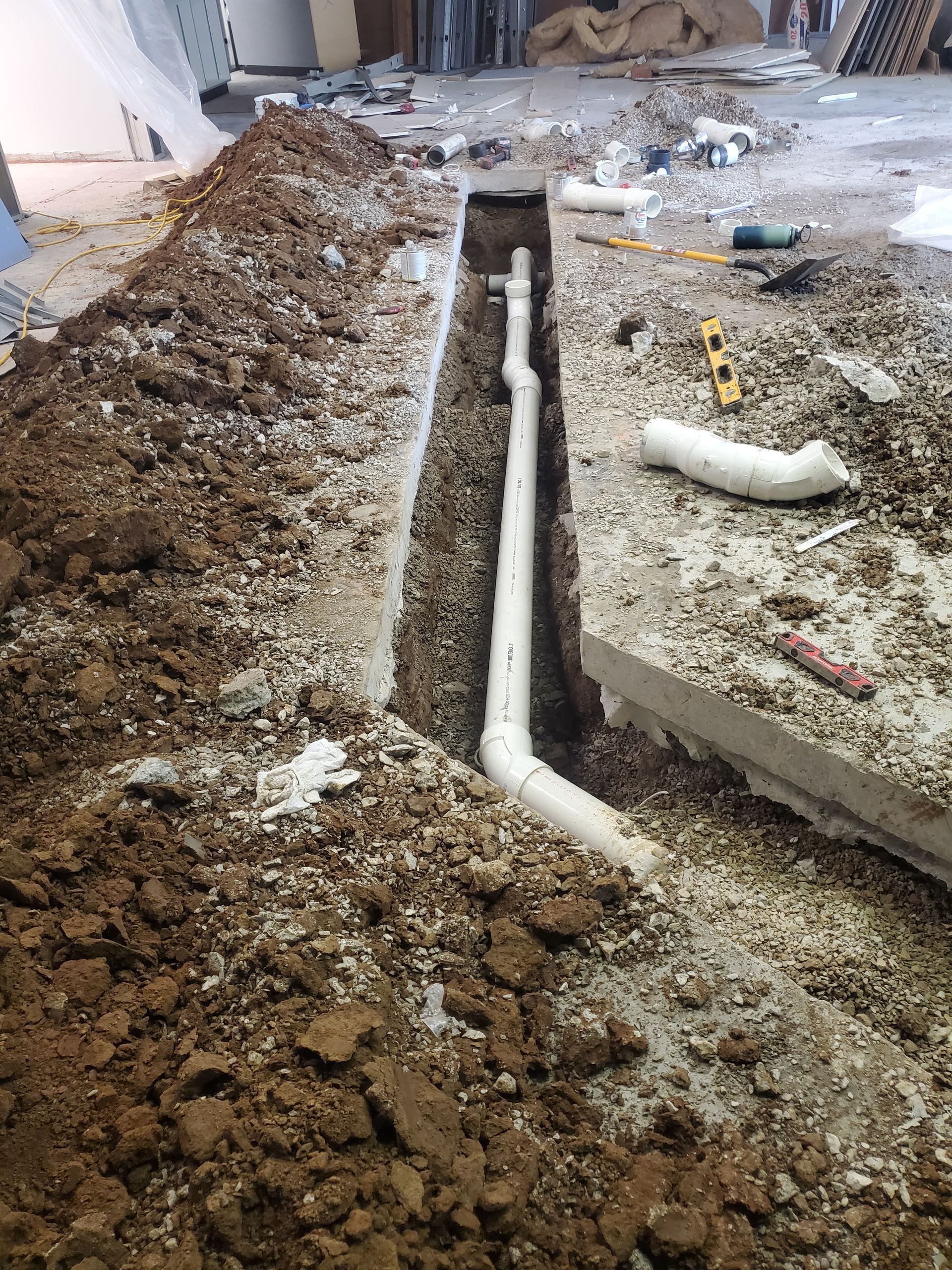 Construction trench with exposed white PVC pipe running through gravel and dirt floor